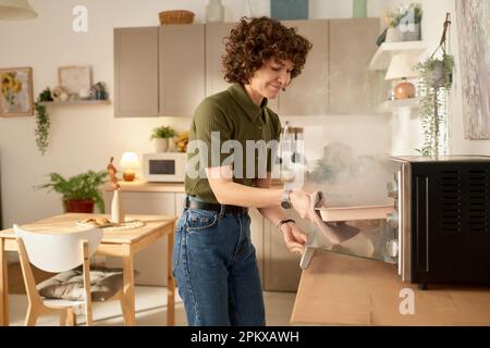 Young housewife taking burnt food out of the oven during cooking in the kitchen at home Stock Photo