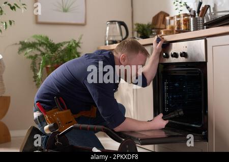 Professional worker examining the problem with oven and repairing it during his visit to home Stock Photo