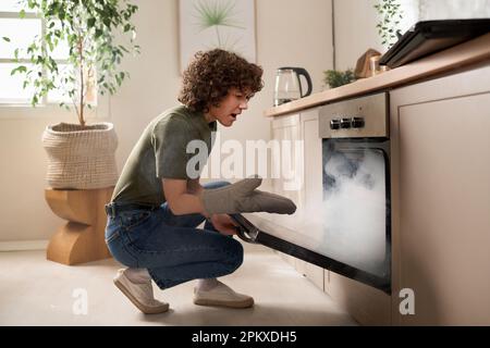 Housewife opening the oven door and taking out burnt food during her cooking in the kitchen Stock Photo