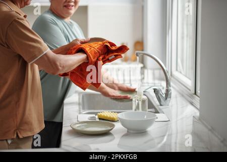 Senior woman washing dished and husband wiping with sof towel Stock Photo