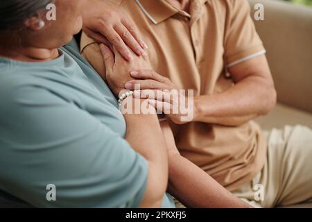 Hands of senior couple touching each other with love and tender when cuddling on couch at home Stock Photo