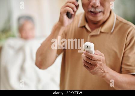 Aged man calling ambulance after measuring body temperature of his wife Stock Photo