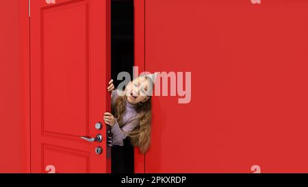 Cute, beautiful little girl, kid in birthday accessories peeking out red door with surprised face. Cheerful celebration Stock Photo