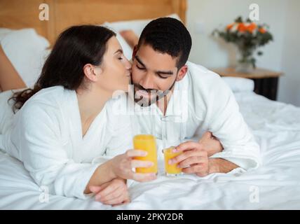 Wife Kissing Husband's Cheek Drinking Juice Relaxing In Hotel Room Stock Photo