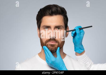 Middle aged man getting marks on face for cosmetic surgery, plastic surgeon applying marks on male face before surgery Stock Photo