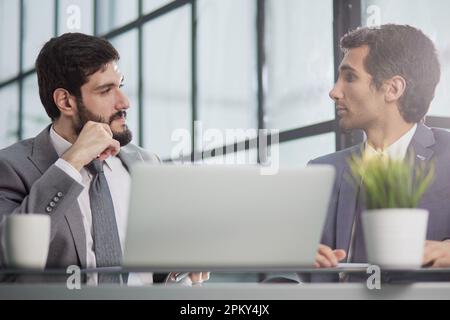 Portrait of two diverse colleagues sitting at desk and using laptop computers Stock Photo
