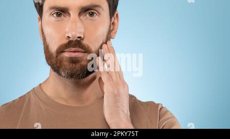 Headshot portrait of middle aged man touching beard and looking at camera over blue background, panorama, free space Stock Photo