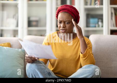Shocked black woman holding papers and gesturing at home Stock Photo