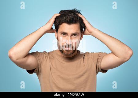 Portrait of handsome bearded middle aged man looking at camera and touching his hair, posing over blue background Stock Photo