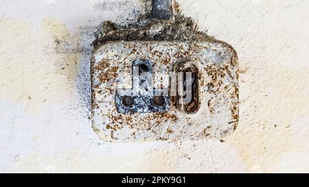 A very old round pin socket covered with rust and dirt on the wall of an old building. Stock Photo