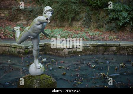 Broken statue of Hermes in an out of focus pond in woodland area of Peasholm Park in Scarborough Stock Photo