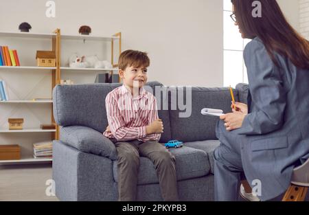 Happy little boy sitting on the sofa and talking to a woman therapist or psychologist Stock Photo