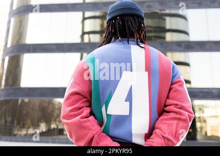 Back view of anonymous black male with braids standing near fence in city street Stock Photo