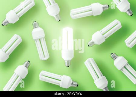 Set of CFL light bulbs arranged around glowing one on green background representing concept of leading idea Stock Photo