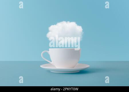 Cloud floating above white ceramic cup of aromatic drink representing concept of thoughts during coffee break on blue background Stock Photo