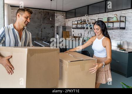 Happy young couple in casual clothes smiling and carrying carton boxes with belongings during relocation to new apartment Stock Photo