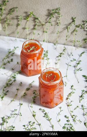Jars filled with homemade fruit jam placed on table with green sprigs of thyme Stock Photo