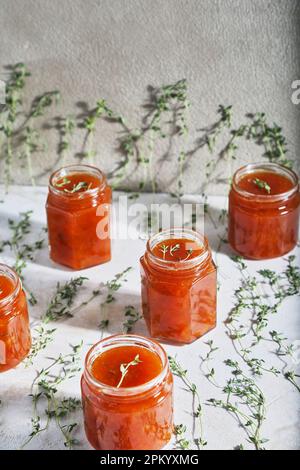 Jars filled with homemade fruit jam placed on table with green sprigs of thyme Stock Photo