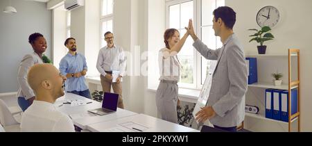 Joyful colleagues give each other high five in office after successfully completed work together. Stock Photo