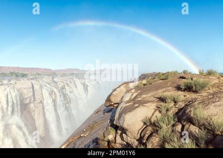 A rainbow is visible over tourists at a viewpoint at the Augrabies waterfalls in the Orange River. The river is in flood Stock Photo