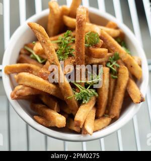 A white bowl filled with fresh, golden-brown French fries, topped with fresh parsley Stock Photo