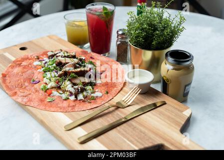 A closeup of a freshly-made Mexican dish made from tortilla and topped with grilled chicken, vegetables and a special sauce Stock Photo
