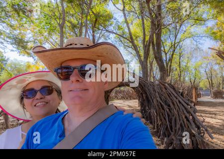 Man with his woman behind smiling against green foliage and blue sky, enjoying in public park, tunnel made of tree branches and wooden poles in backgr Stock Photo