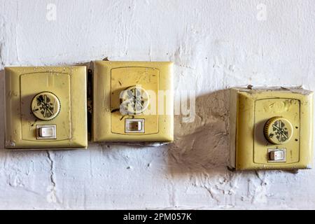 Misaligned old dirty switches for on, off and speed control of ceiling fans against a white wall, small yellow plastic boxes, rough textured wall Stock Photo