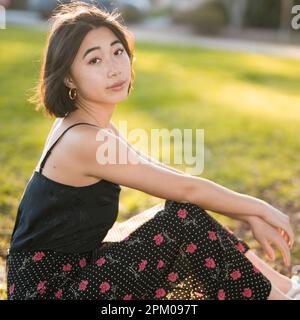 Young Asian Woman Seated on Grass in a Palo Alto Park | Backlit | Moody | Warm Tones Stock Photo