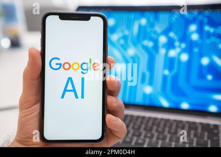 The smartphone screen held by a man shows a Google AI neural network logo, while in the background, a laptop displays a splash screen with a neuronet. March 2023, Prague, Czech Republic  Stock Photo