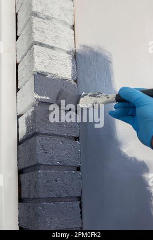 Man painting interior bricks with blue paint using a brush. Do it yourself home improvement concept Stock Photo