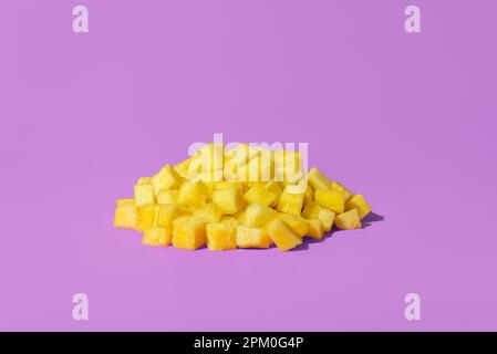 Pile of pineapple cubes minimalist on a purple background. Fresh pineapple sliced in small pieces, in bright light on a vibrant colored table Stock Photo