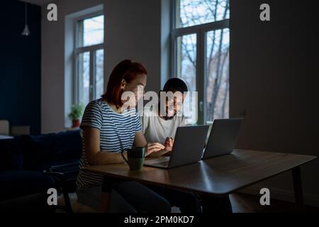 Smiling multiracial family couple enjoy freelancing, sitting at table working on laptops together Stock Photo