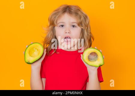 Kid hold red avocado in studio. Studio portrait of cute child with avocado isolated on yellow background Stock Photo