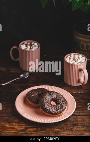 Two Chocolate Donuts and Two Mugs of Hot Chocolate with Marshmallow on Rustic Wooden Table Stock Photo