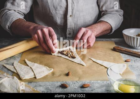 Homemade croissant preparing. Baker rolls the puff pastry stuffed with chopped almonds and hazelnut spread Stock Photo