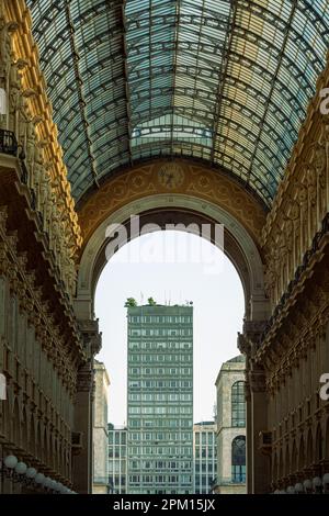 A building with a glass roof is visible through a tunnel that has a glass roof - Italy, Lombardy, Milan Stock Photo