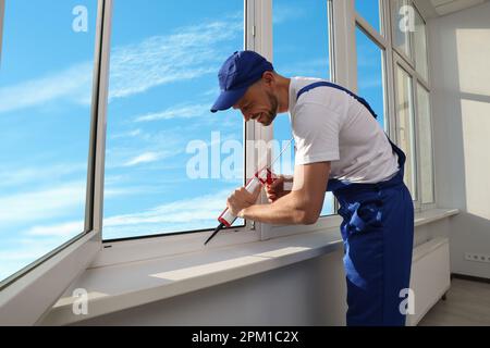 Worker sealing plastic window with caulk indoors. Installation process Stock Photo
