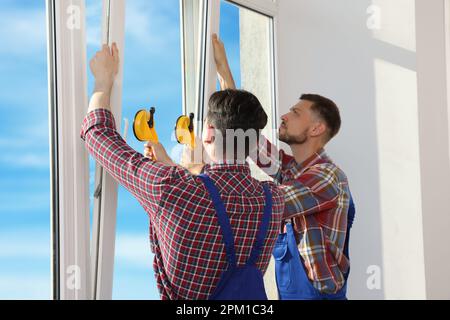 Workers using suction lifters during plastic window installation indoors Stock Photo