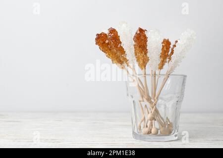 Sticks with sugar crystals in glass on white wooden table, space for text. Tasty rock candies Stock Photo