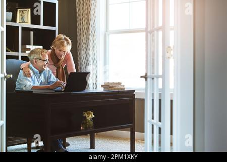 Doing their budget together. a mature woman keeping her husband company while he works from home. Stock Photo