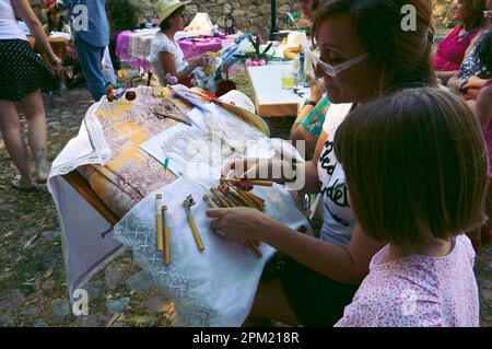 Brihuega, Spain - July 16, 2012. A woman making bobbin lace while a little girl watches attentively Stock Photo