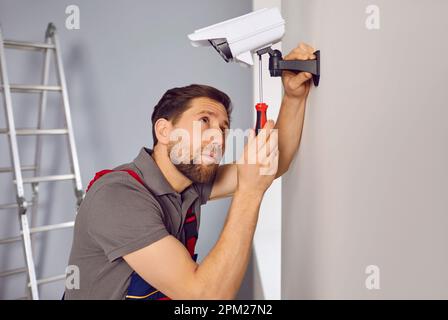 Man worker setting up a surveillance camera on the wall inside the house or apartment Stock Photo