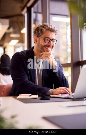 Mature Businessman Wearing Glasses Working On Laptop At Desk In Office Stock Photo
