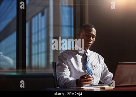 Doing all the necessary research for his case. a businessman taking notes while using his laptop. Stock Photo