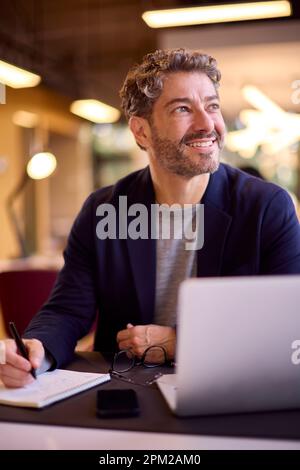 Mature Businessman Working At Desk In Office Writing In Notebook Stock Photo