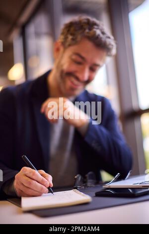 Mature Businessman Working At Desk In Office Writing In Notebook Stock Photo