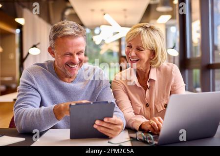 Mature Male And Female Business Colleagues Meeting Using Laptop And Digital Tablet In Modern Office Stock Photo