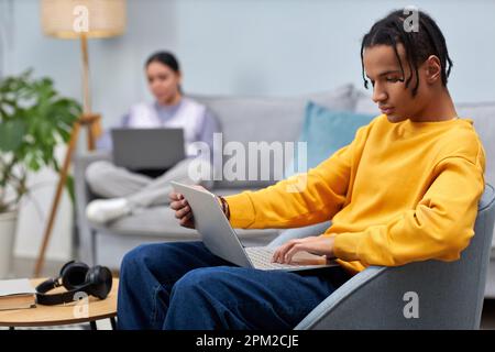 Portrait of black young man using laptop while sitting on sofa in office lounge Stock Photo