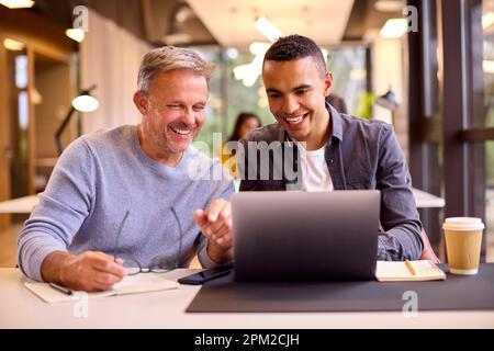 Mature Businessman Mentoring Younger Colleague Working On Laptop At Desk Stock Photo